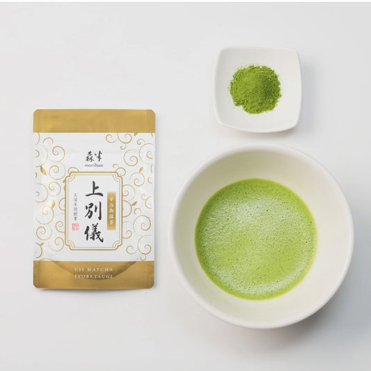 Matcha green tea packaging, bowl of matcha, and scoop of matcha on a white background